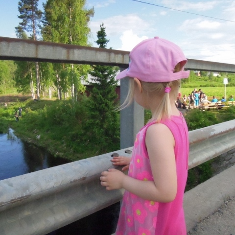 Pieni tyttö seisoo sillalla ja katselee jokea