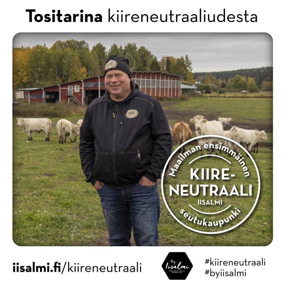 Kuvassa virnistävä Antti Niskanen seisoo laitumella. Taustalla näkyy useamman lehmän lauma ja pihattonavetta kauniissa maalaismaisemassa.